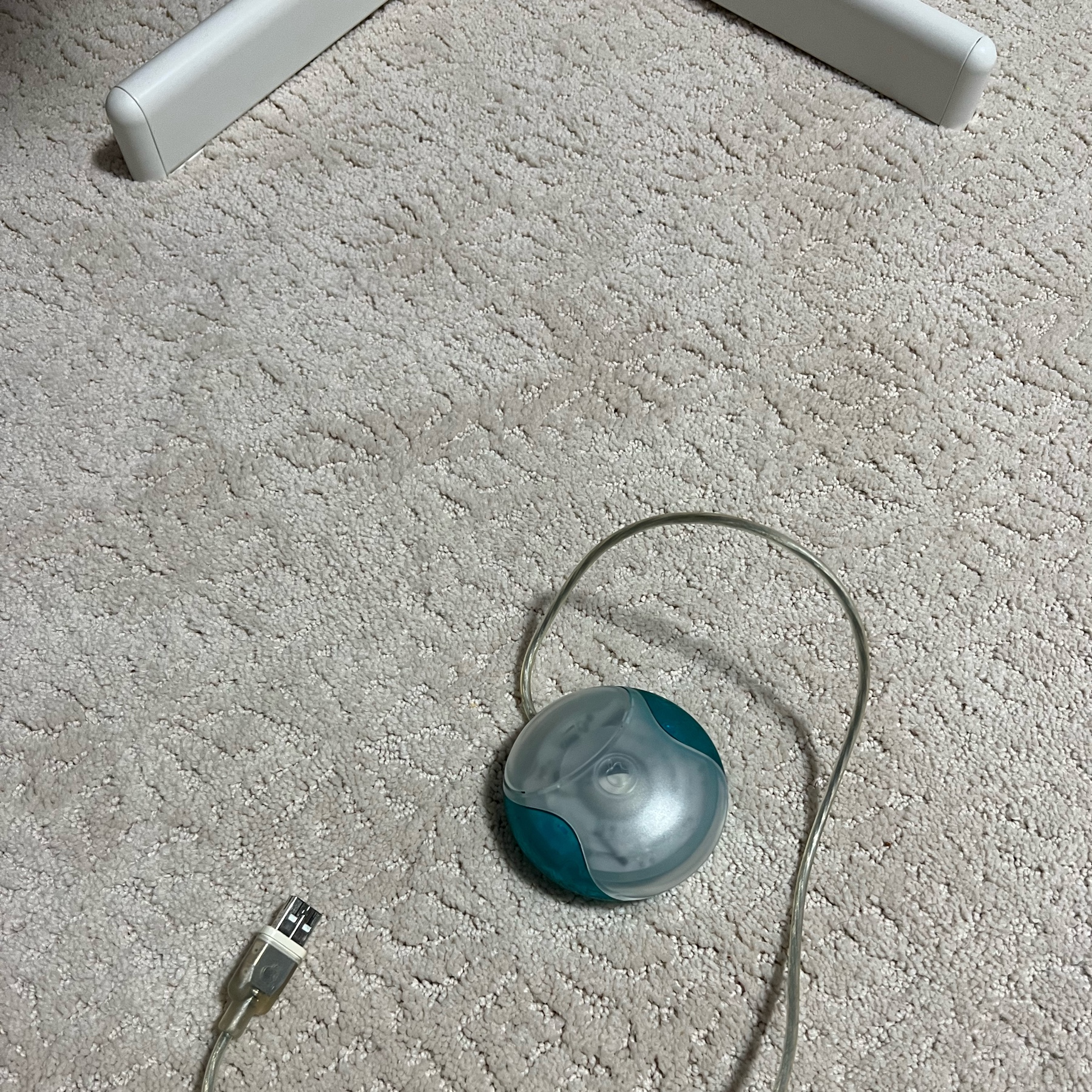 A blue and white USB puck mouse sitting on beige carpet
